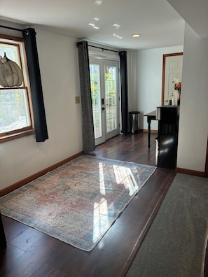 A spacious room with a large rug, a wooden floor, a door with glass panels, and a small table with a vase. - Spacious 1 bedroom
Suite. Private Entrance (Clifton park)