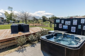 Un bain à remous doté d’une terrasse en bois et d’une zone délimitée par une clôture, où sont placés divers panneaux.