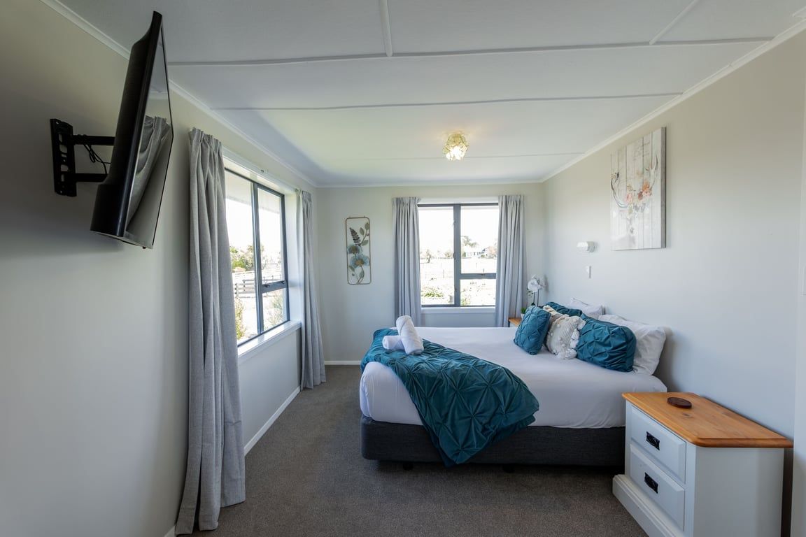 Une chambre à coucher comprenant un lit, une table de chevet, des rideaux et un téléviseur fixé au mur.