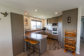 Une cuisine moderne dotée d’un îlot central, de tabourets de bar, d’un four à micro-ondes, d’un four traditionnel et d’un présentoir en bois pour les fruits et légumes.