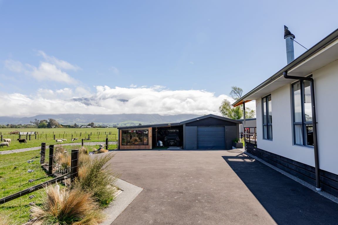 Un bâtiment moderne doté d’un garage, d’un espace extérieur couvert et offrant une vue sur un champ verdoyant où paissent des moutons.