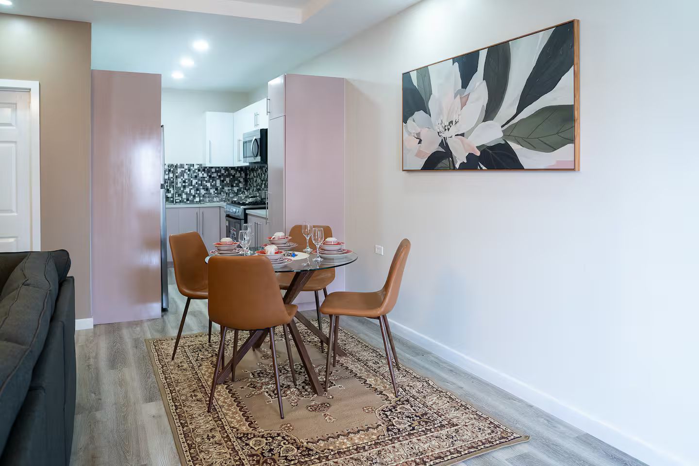 A dining area with a table set for four, surrounded by chairs, and a kitchen in the background.