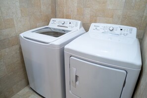 Deux machines à laver à chargement frontal, de couleur blanche, se trouvent dans une salle de bain dont les murs sont recouverts de carreaux beiges.