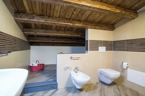 Een badkamer met een houten plafond, een bidet, toilet en een bad.