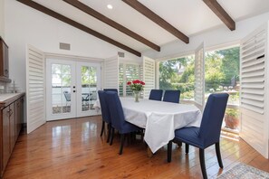 Uma área de refeições com uma mesa branca, cadeiras azuis e vista para o exterior.