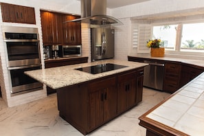 Cozinha moderna com ilha central, eletrodomésticos de aço inoxidável e vista para o exterior.