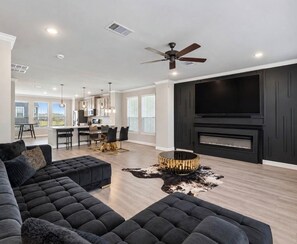 A modern living room with a sectional sofa, a round coffee table, a fireplace, and a television. - The Skyline Retreat: 3-Story Luxury Near Downtown (Houston)
