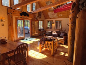 Ein rustikales Interieur einer Lodge mit einem Holzespeisetisch, einem Ledersofa und einer großen Holztür, die nach draußen führt.