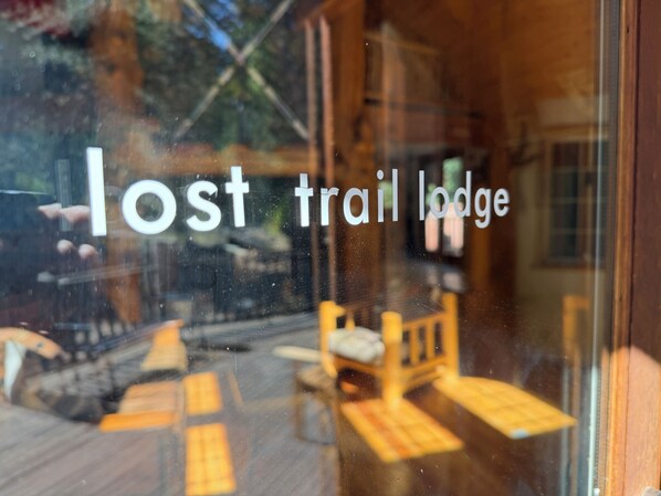 Ein Fenster mit dem Schriftzug 'lost trail lodge' und Blick auf Sitzplätze im Freien.
