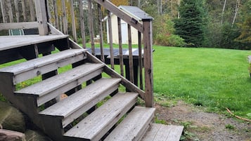 Un escalier en bois mène à une terrasse d’où l’on peut admirer une cour verdoyante et des arbres.