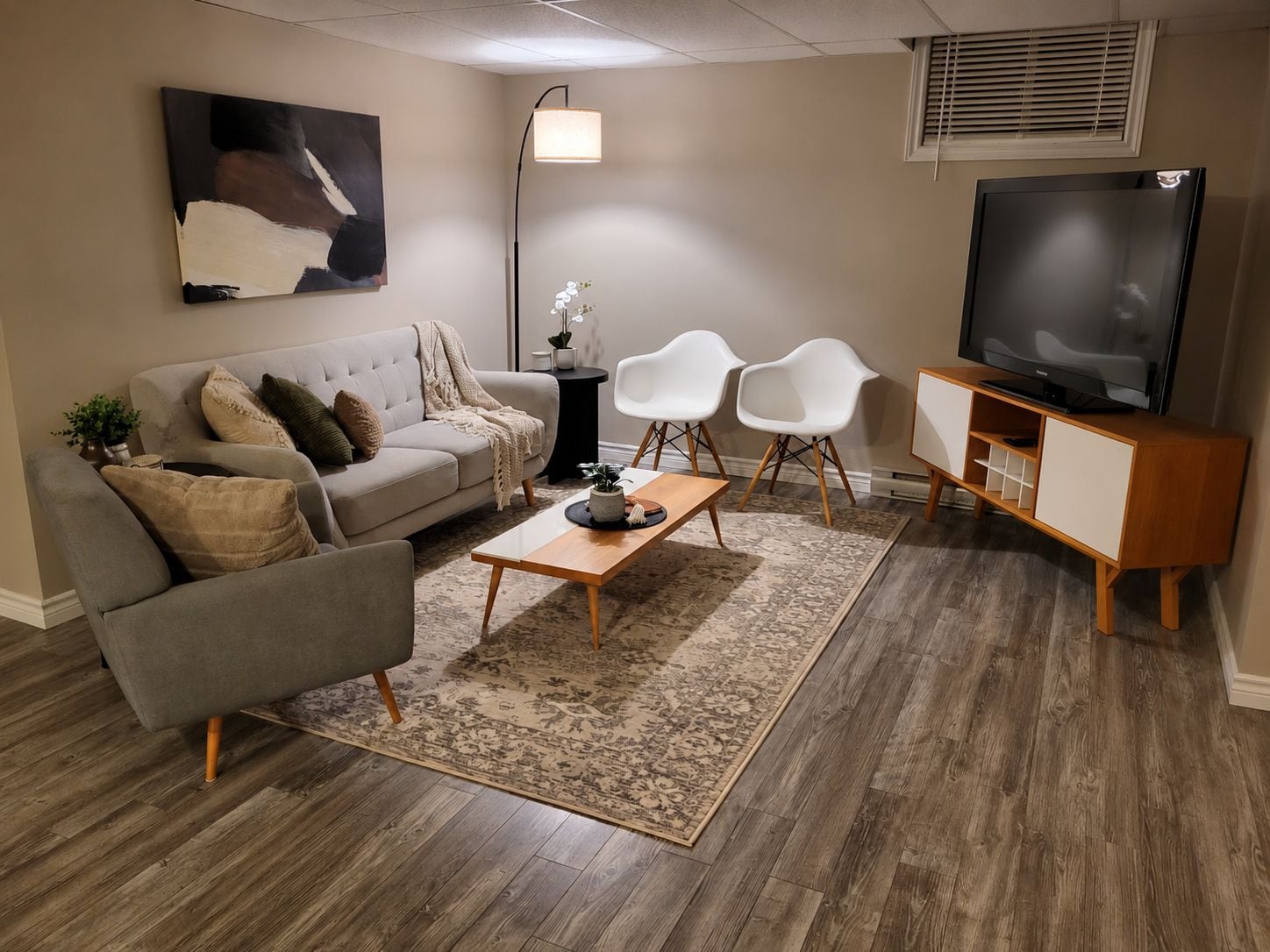 A living room with a sofa, armchair, coffee table, TV, and a painting on the wall.