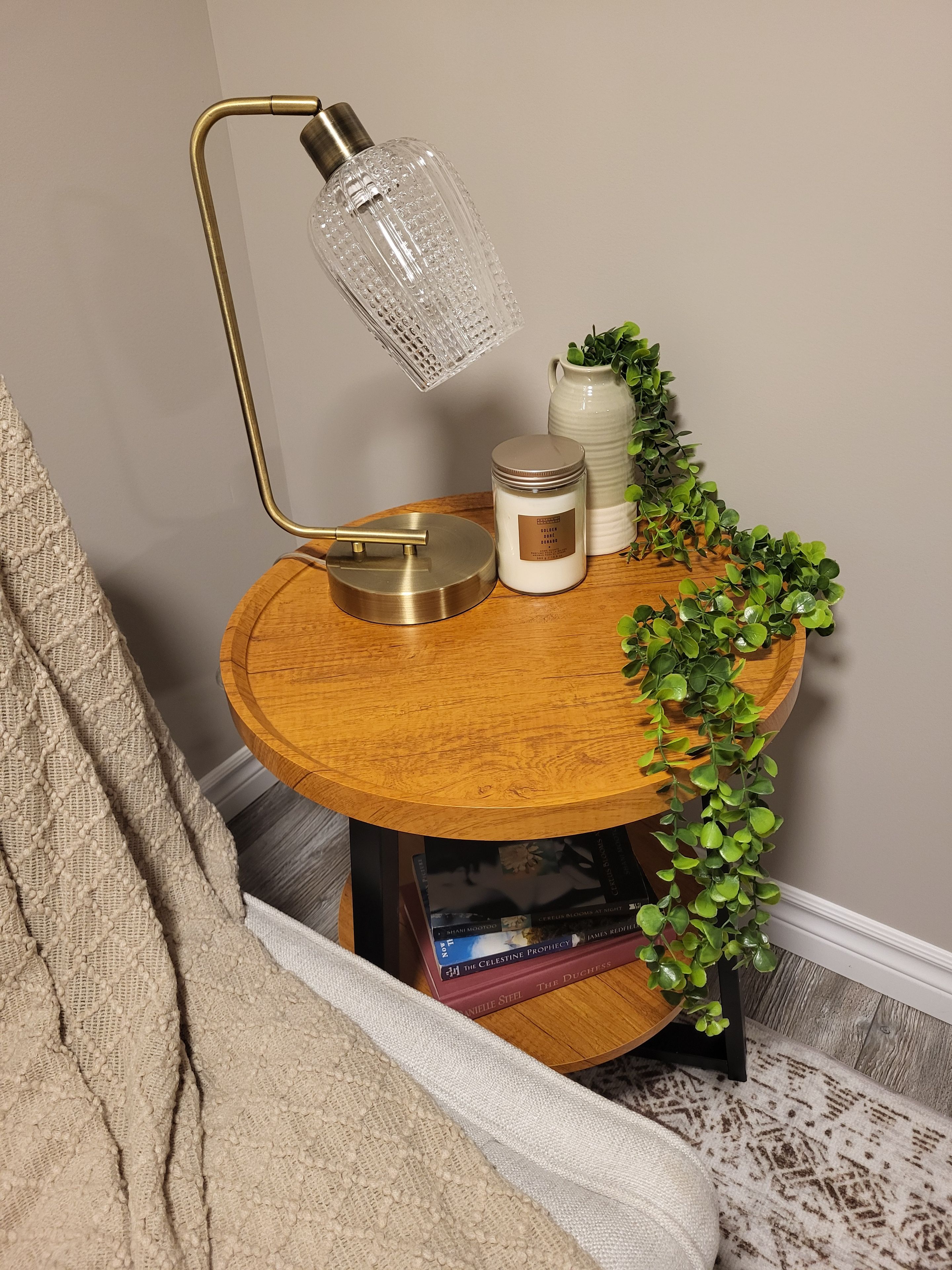 A round wooden side table with a brass lamp, a white candle, and a small potted plant.