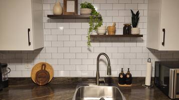 A kitchen with a stainless steel sink, white tiled backsplash, and wooden shelves with decorative items.