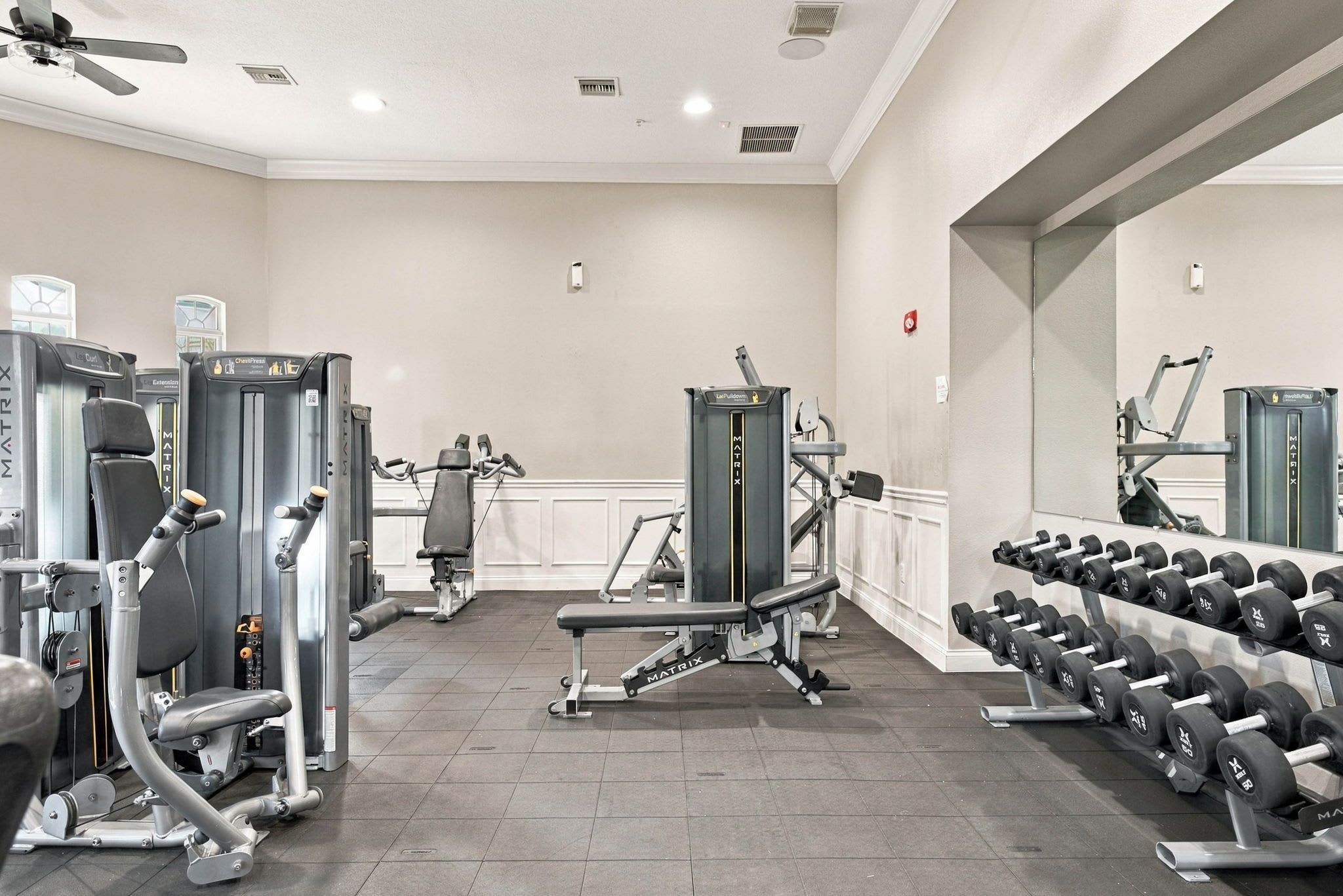 Une salle de sport équipée de divers appareils d’exercice, notamment un banc de développé couché, des haltères et des appareils de cardio.