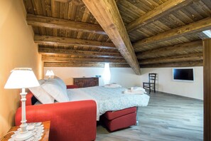 Een slaapkamer met een houten plafond, een bed met een rode kap, een nachtkastje met een lamp, een dressoir en een stoel.