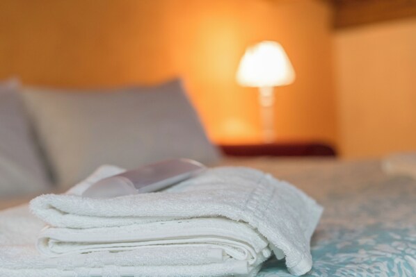 Een netjes opgevouwen witte handdoek op een bed met een geborduurd sprei.