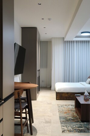 Moderni hotellihuone, jossa on sänky, työpöytä, televisio ja kylpyhuone.