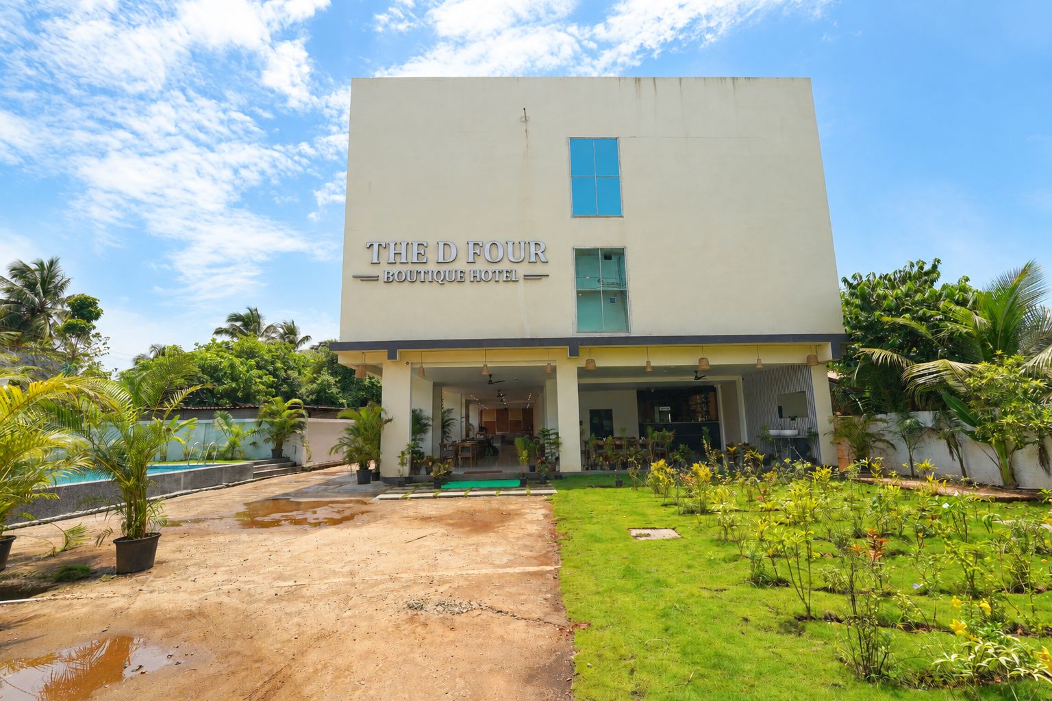 A modern boutique hotel with a flat roof, a large entrance, and a well-maintained garden.