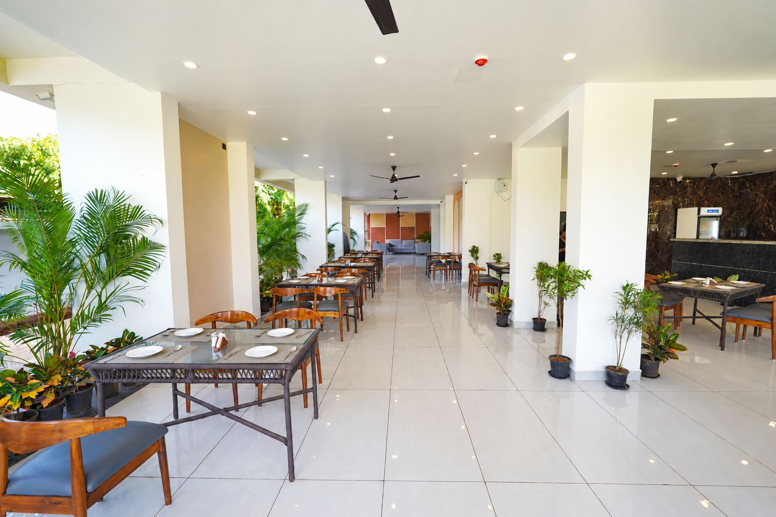 A spacious indoor dining area with multiple tables and chairs, ceiling fans, and potted plants.