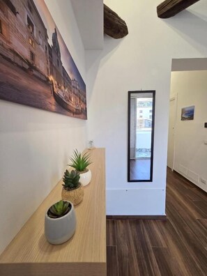 A hallway with a wooden reception desk, potted plants, a framed picture on the wall, and a view through a window. - Angelina Rooms (Palermo)