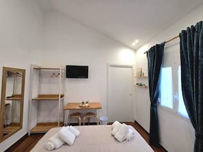 A hotel room with a bed, a desk, a chair, a TV, a wardrobe, and a window with curtains. - Angelina Rooms (Palermo)
