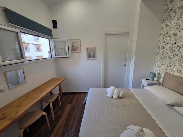 A hotel room with a bed, a desk, a chair, and a door. - Angelina Rooms (Palermo)