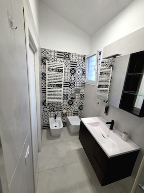 A bathroom with a white sink, two bidets, a mirror, and patterned tiles on the walls. - Angelina Rooms (Palermo)