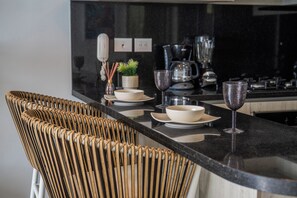 Une cuisine moderne avec un plan de travail noir, des chaises en osier et une machine à café.