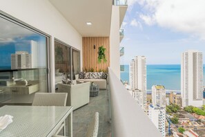 Un balcon avec un canapé, une table en verre et une vue sur l’océan et le paysage urbain.
