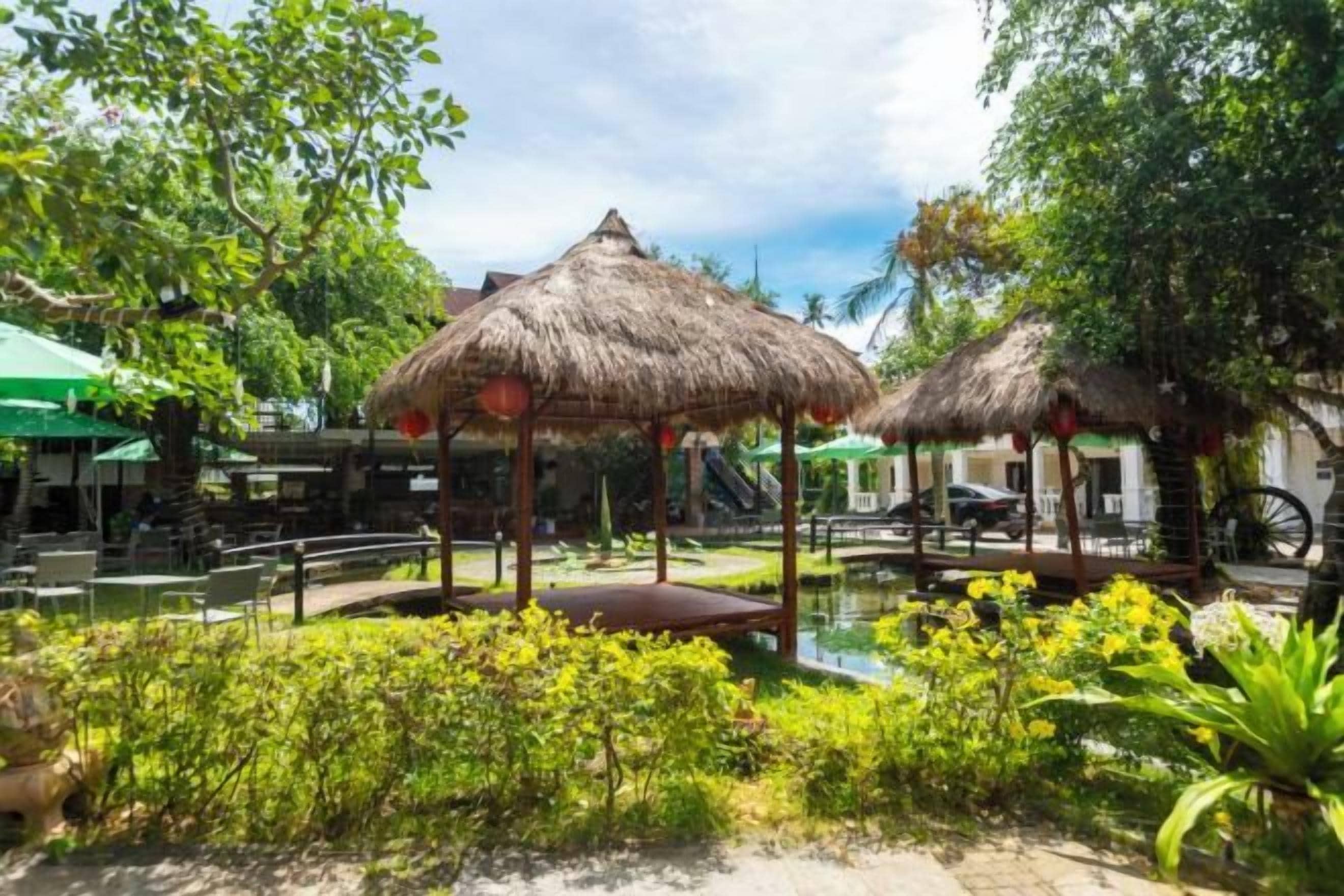 A tropical garden with thatched umbrellas, a small pond, and lush greenery.