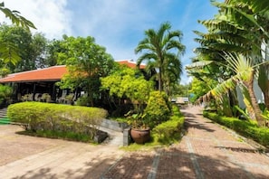 A pathway lined with potted plants and palm trees, leading to a building with a red roof. - Tahiti Resort (Phu Quoc Island)