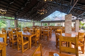 An indoor dining area with wooden tables and chairs, a brick pillar, and a high ceiling with metal beams. - Tahiti Resort (Phu Quoc Island)