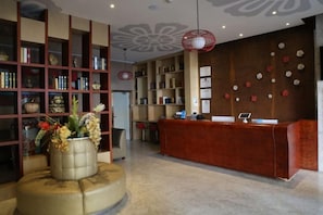 A reception area with a red desk, a bookshelf, and a decorative vase. - Qingya Hotel (Zhengzhou)