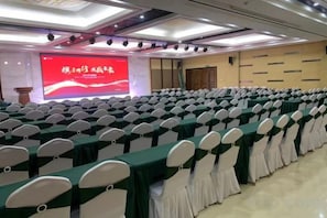 A conference room with rows of tables and chairs, a large screen, and a podium. - Qingya Hotel (Zhengzhou)