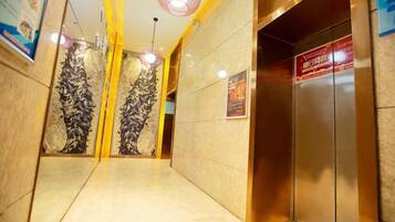 A hotel corridor with a marble wall, an elevator, and a ceiling light fixture.