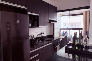 A modern kitchen with dark cabinetry, a stainless steel refrigerator, and a window providing a view of the city. - New Listing (Praia Grande)