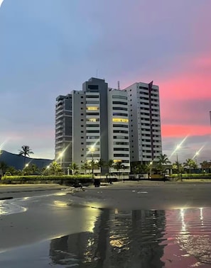 A multi-story building with balconies, located near a body of water reflecting lights. - New Listing (Praia Grande)