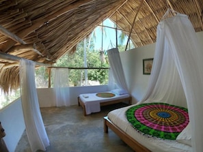 A room with a bed, a bench, and a view of greenery outside.