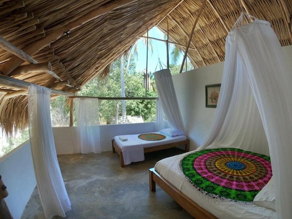 A room with a bed, a bench, and a view of greenery outside.