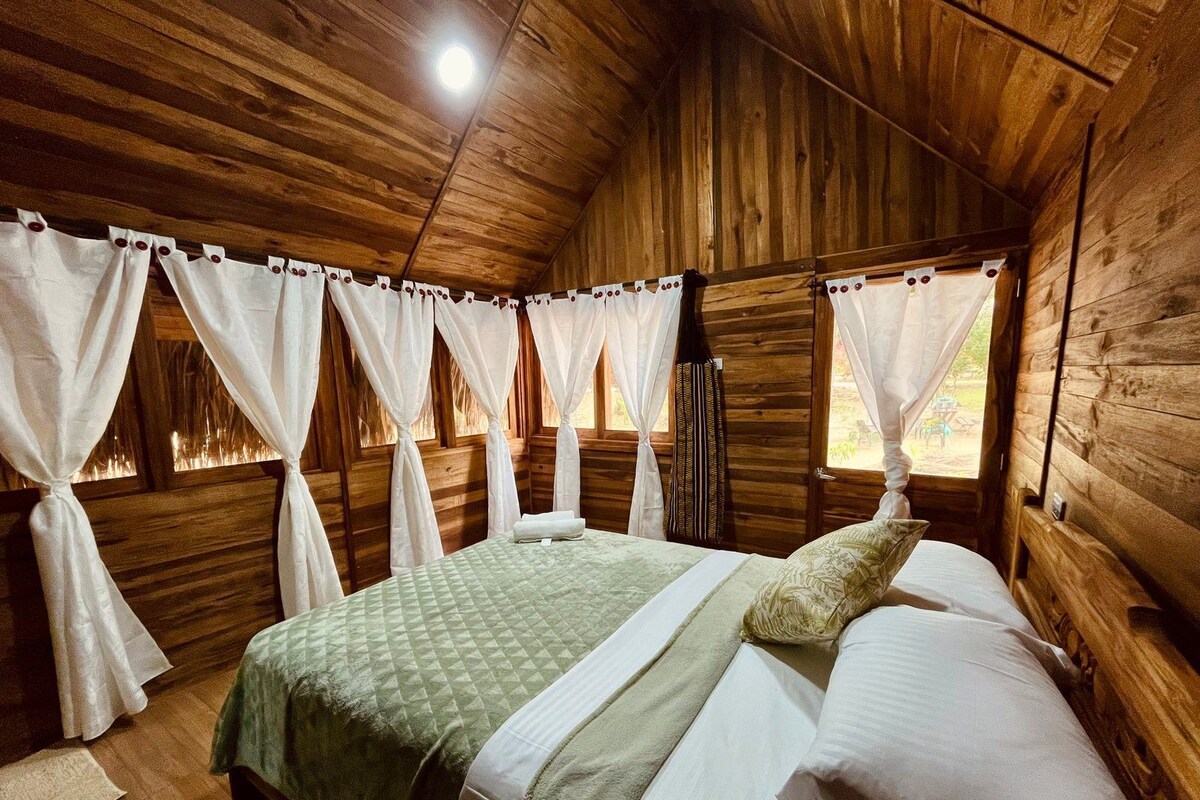 A wooden room with a bed, curtains, and a window.