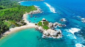 A coastal area with a beach, rocky outcrops, and clear turquoise waters.