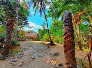 A pathway leading to a thatched-roof structure surrounded by tropical vegetation.