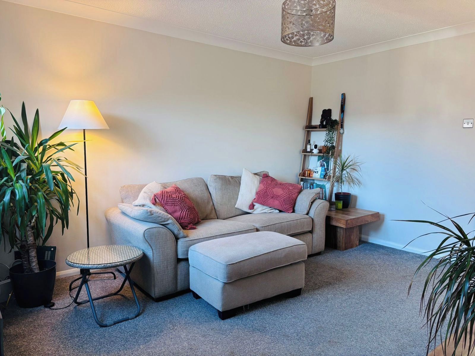 Un salon comprenant un canapé, une petite table ronde, une lampe et une étagère sur laquelle sont disposés divers objets.