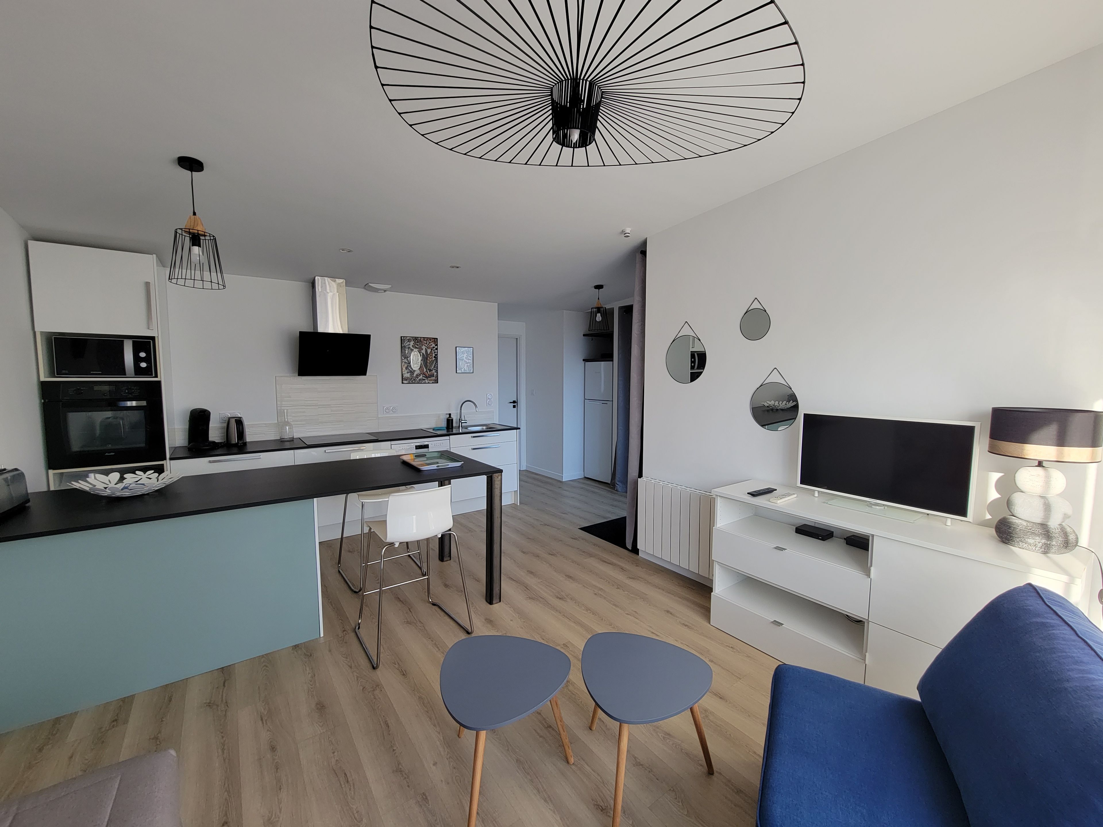 A modern kitchen with a black countertop, white cabinets, and a built-in oven. There is a dining area with a blue sofa and two small tables.
