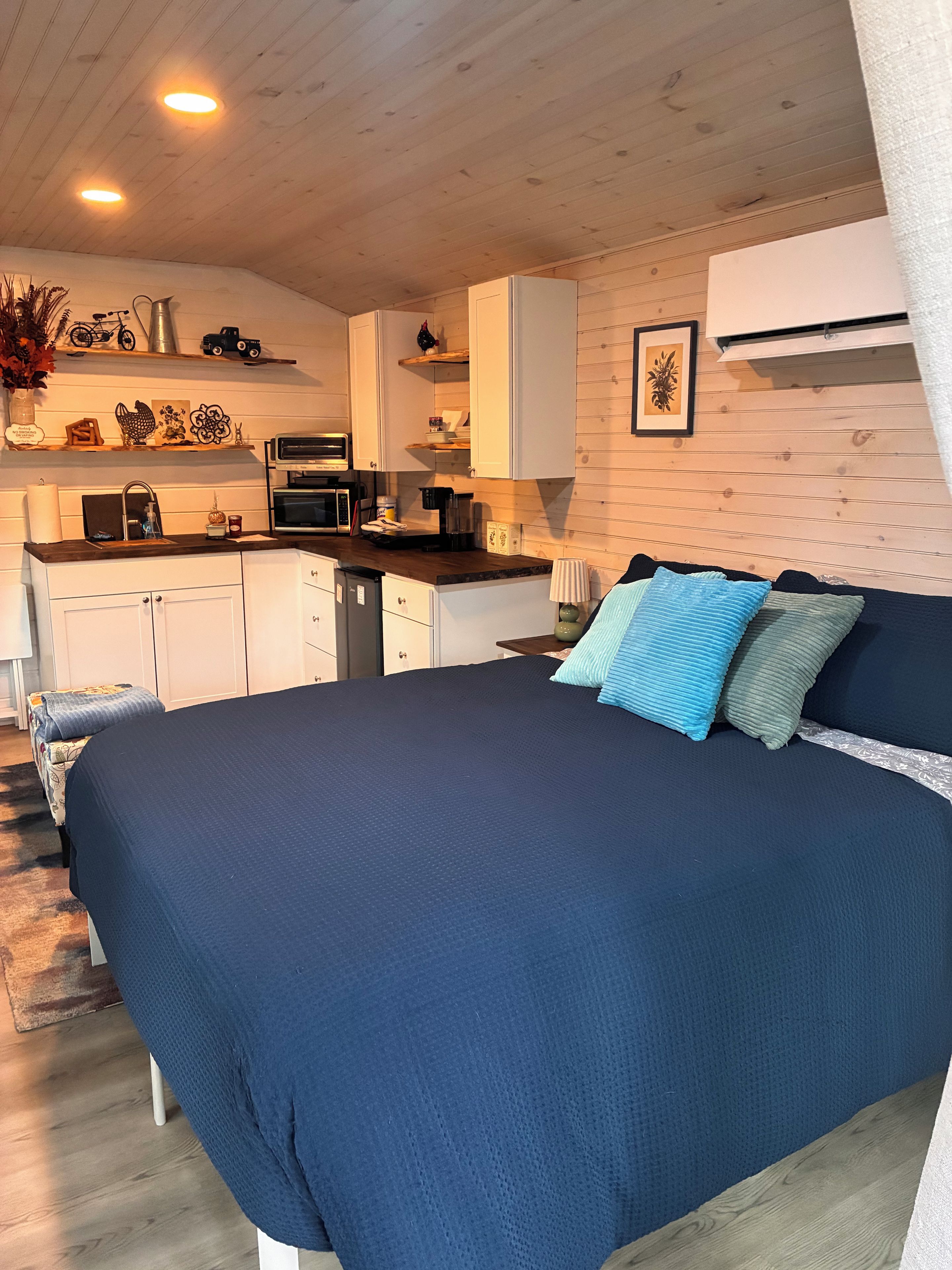 A room with a bed, a kitchenette, and a wooden ceiling.