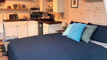 A room with a bed, a kitchenette, and a wooden ceiling.