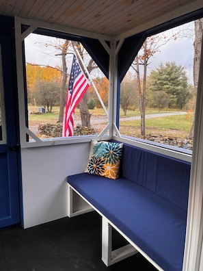 A covered porch with a bench and a view of a flag.