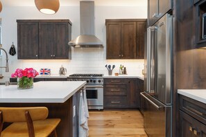 A modern kitchen with dark wood cabinets, stainless steel appliances, and a white island. - Designer & Luxury Modern 3-Bed Penthouse w/Elevator in Truckee w/Hot Tub/Gym (Truckee)