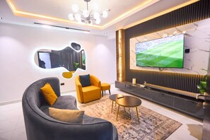 Ein modernes Wohnzimmer mit einem großen Flachbildfernseher an der Wand, einer Couch, einem Couchtisch und einem gemusterten Teppich.