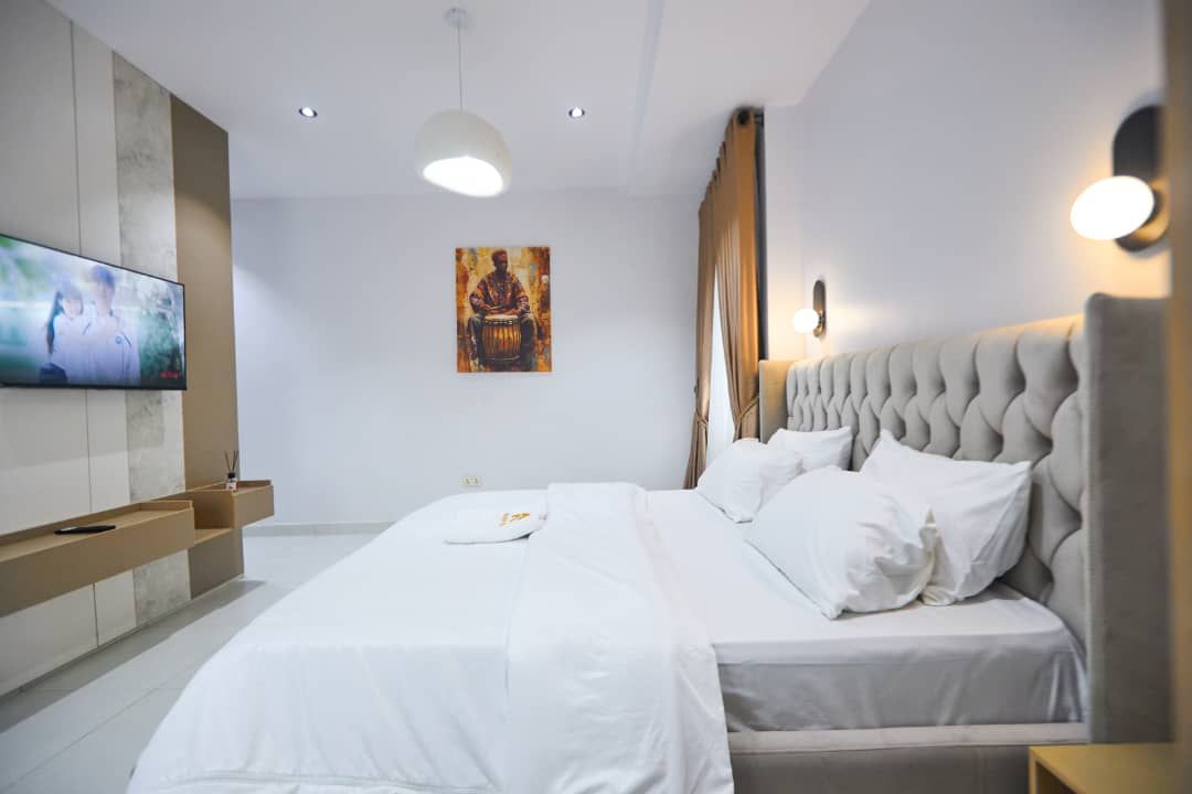 Habitación de hotel moderna con una cama grande, un televisor de pantalla plana, un cuadro en la pared y un banco empotrado.